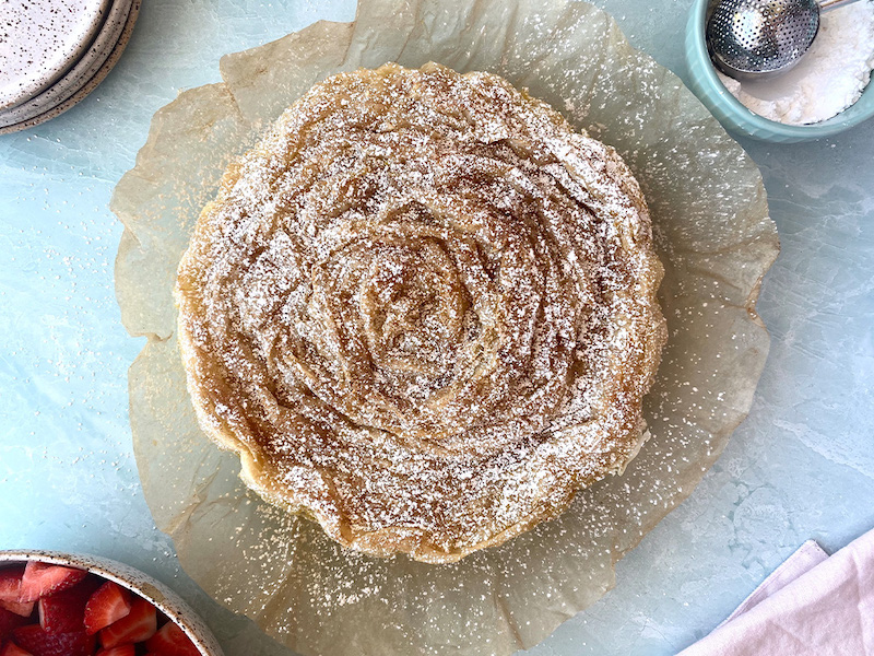 A ruffled milk pie served with powdered sugar and fruit
