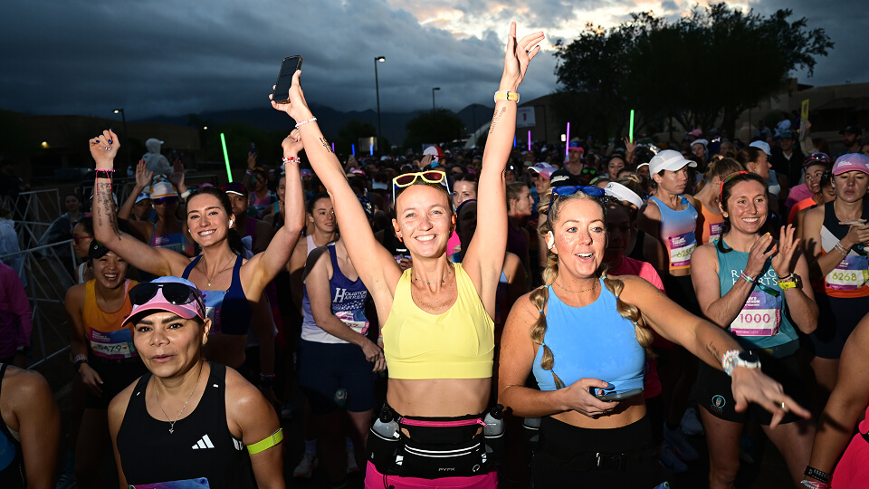 A group of women raise their hands up at the start line of Every Woman's Marathon.